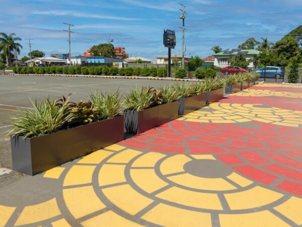 Dark fibreglass commercial trough planter boxes defining a pedestrian zone on a vibrant painted asphalt pavement.