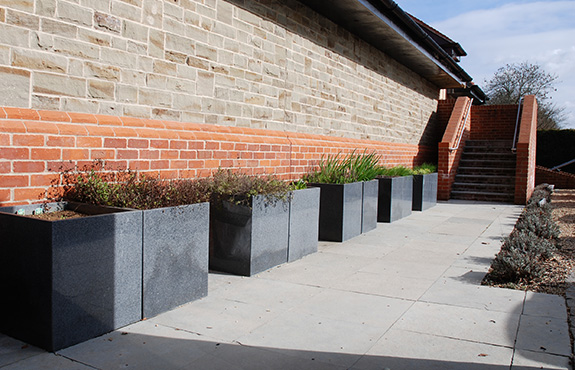 A row of Trough 1000 planters with heather, Tall Taper XXL Planters in background